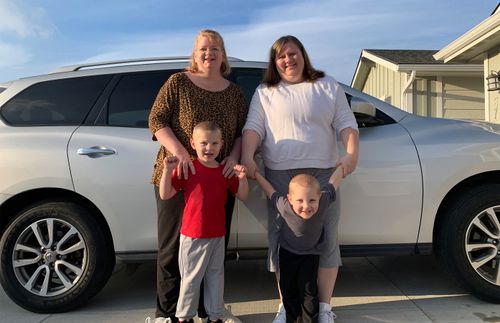 two women and two little boys standing next to a car