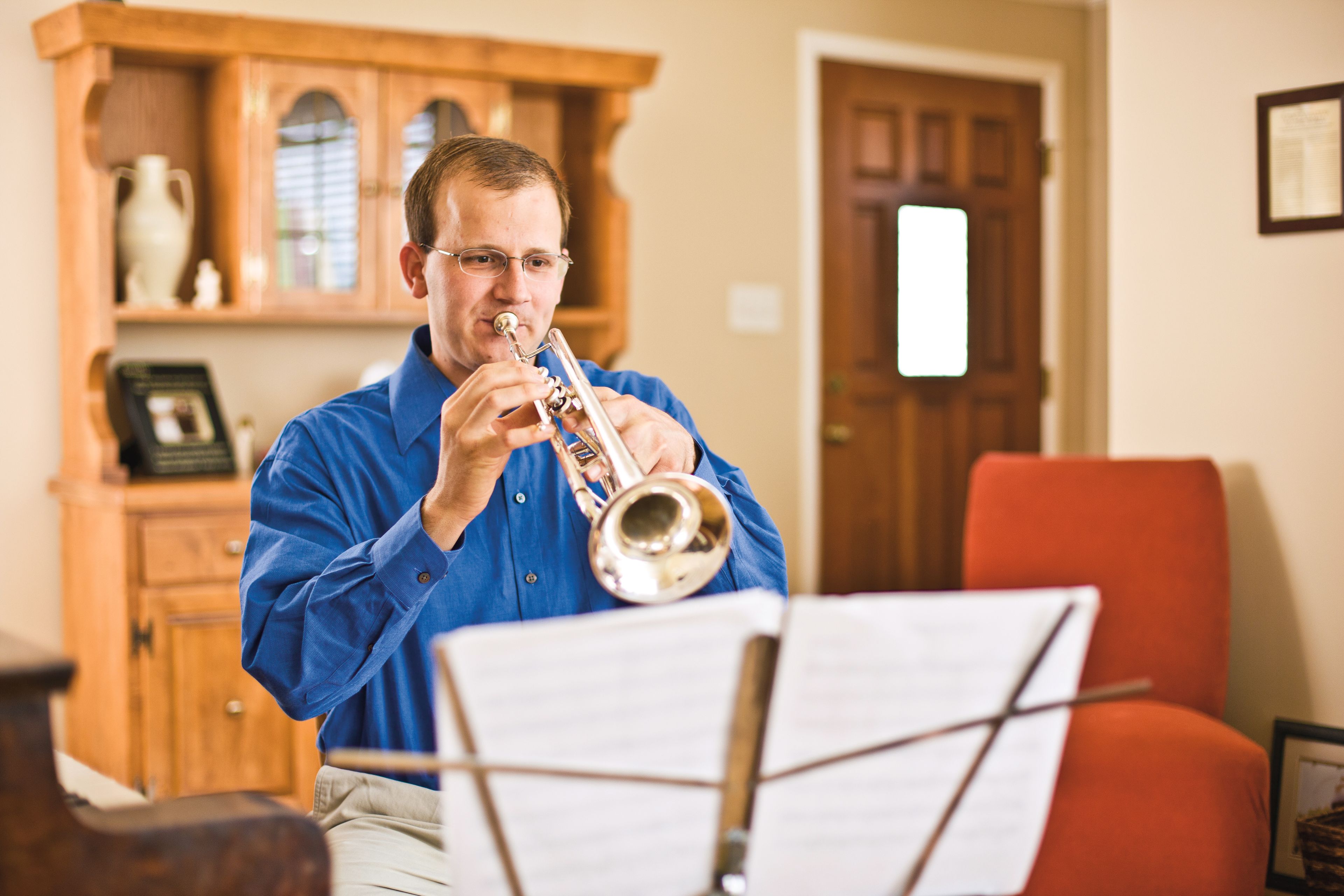 A man plays his trumpet while sitting in the living room.
