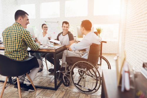 man in wheelchair communicates cheerfully with employees at the office