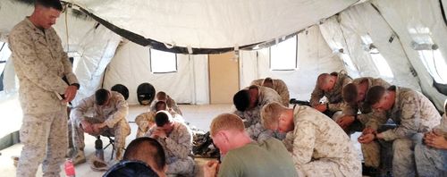 a chaplain praying with servicemen in a tent