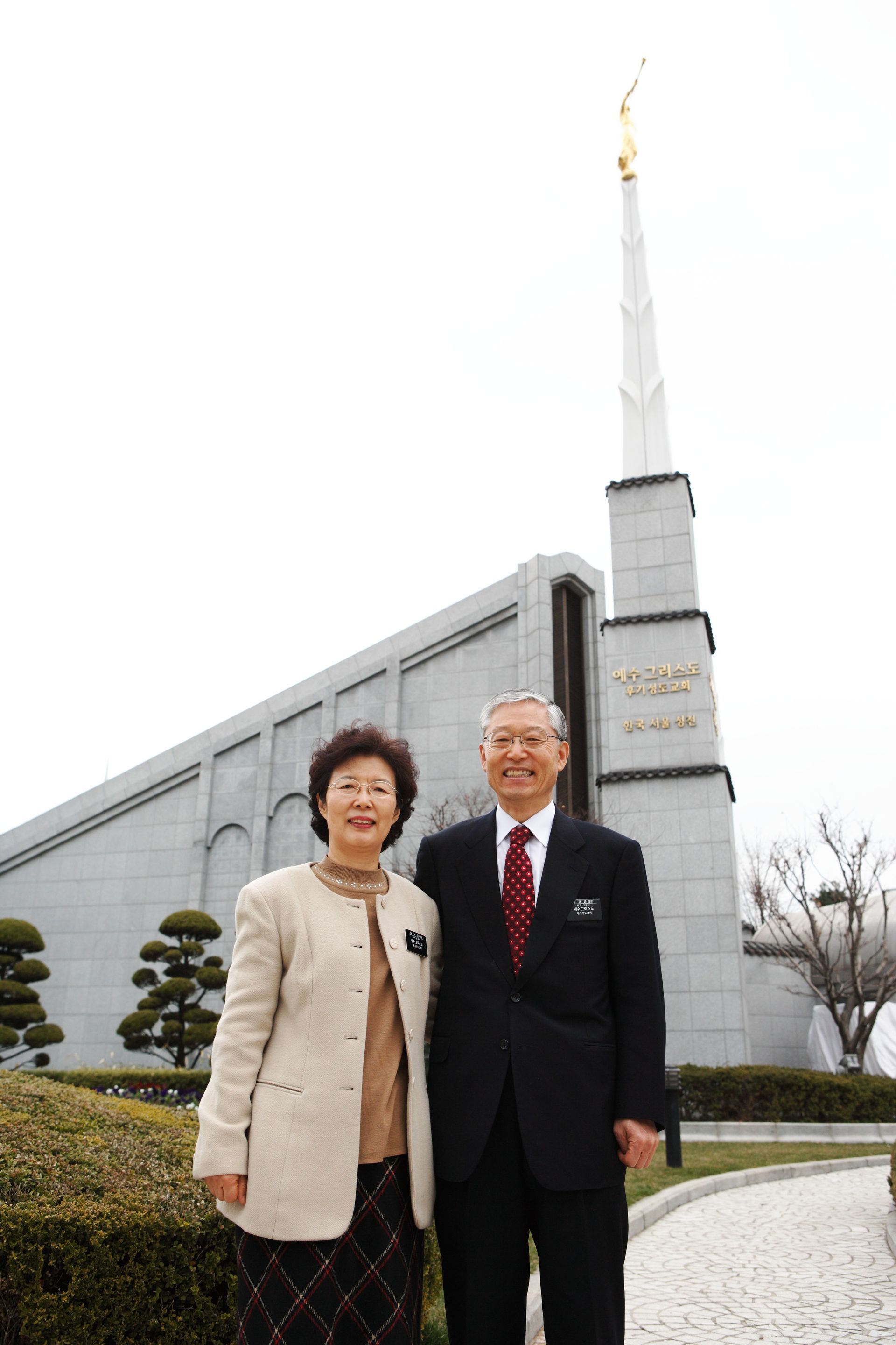 A senior missionary couple standing outside the Seoul Korea Temple.
