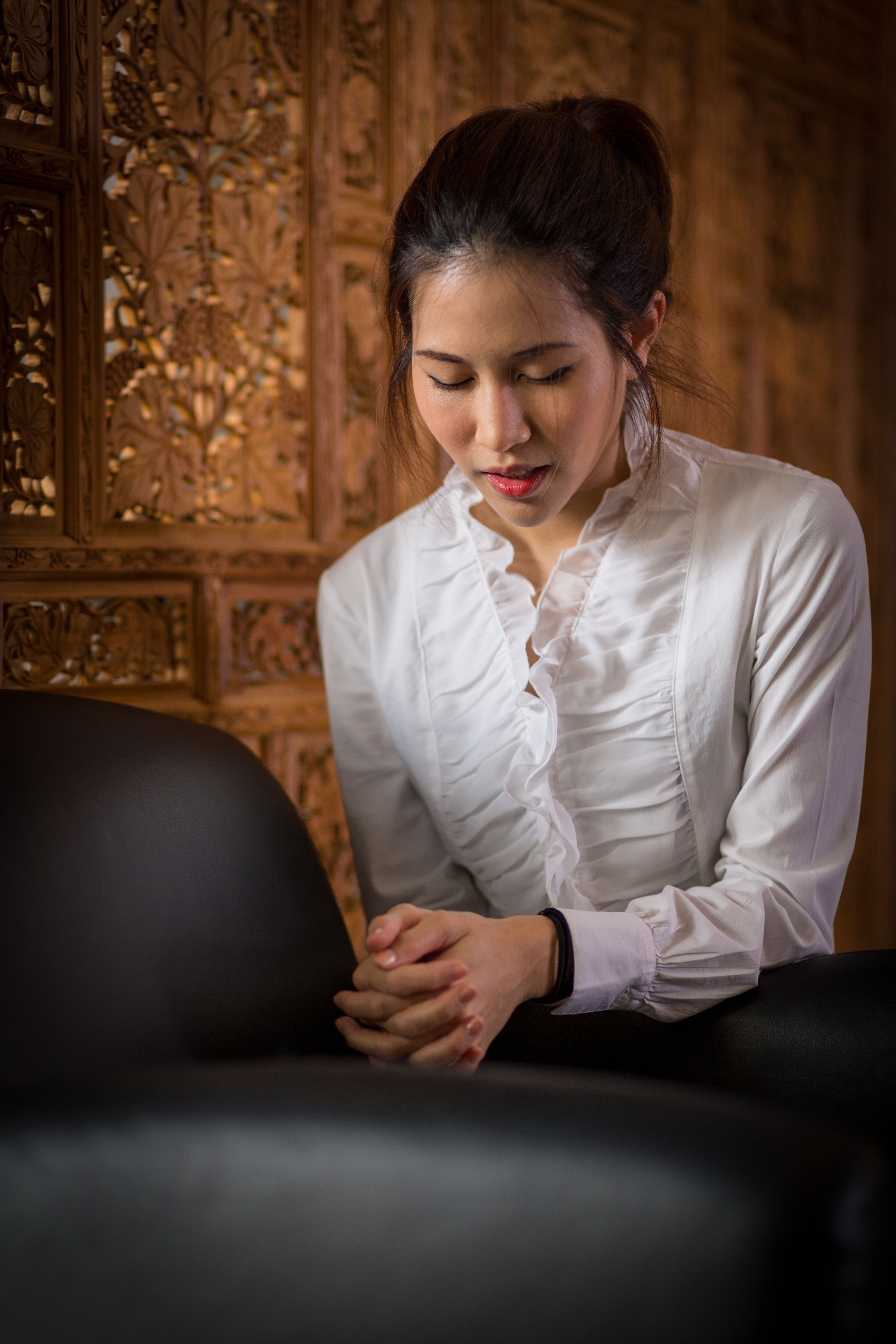 A young woman in Thailand kneels by a chair and prays.