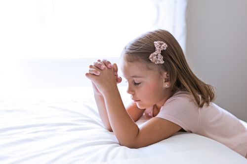 Side view of young girl praying by bed