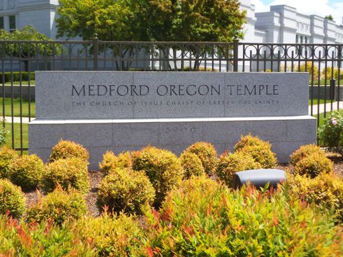 A close-up of the Medford Oregon Temple name sign in front of the temple, beyond the fence surrounding the grounds.
