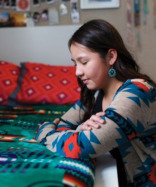 A young woman kneeling beside her bed saying a prayer.