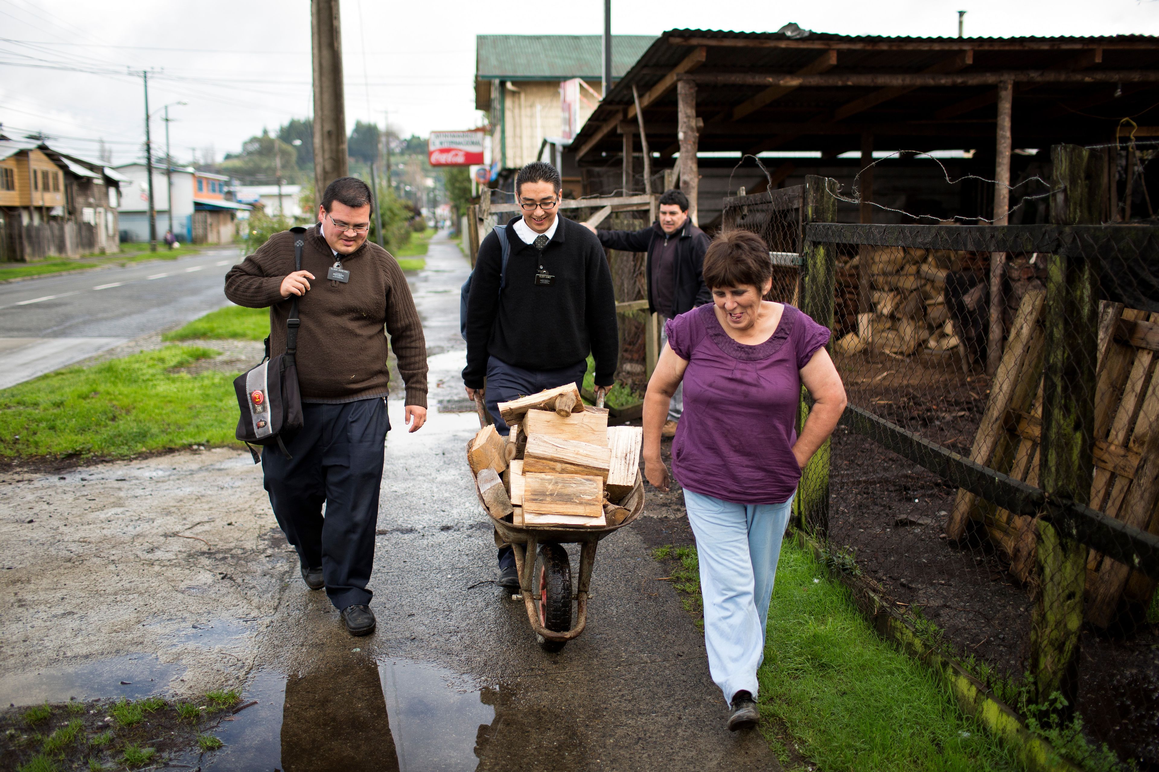Two missionaries help a woman move firewood down the street in a wheelbarrow. Â 