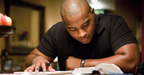 Man sitting at a desk or table looking down at open scriptures.