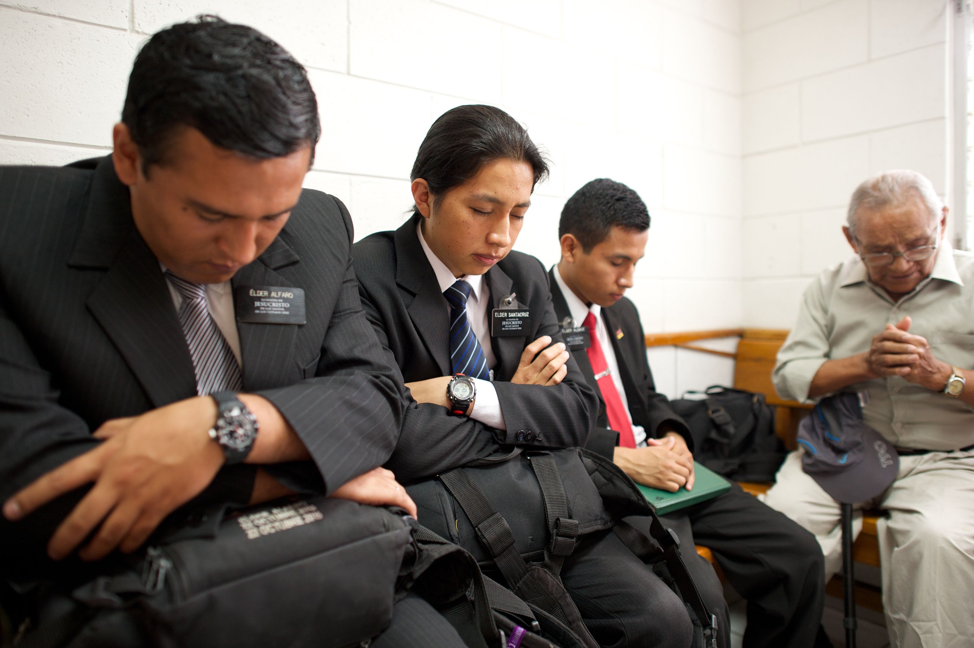 Three elder missionaries sitting and praying in a Church meeting.