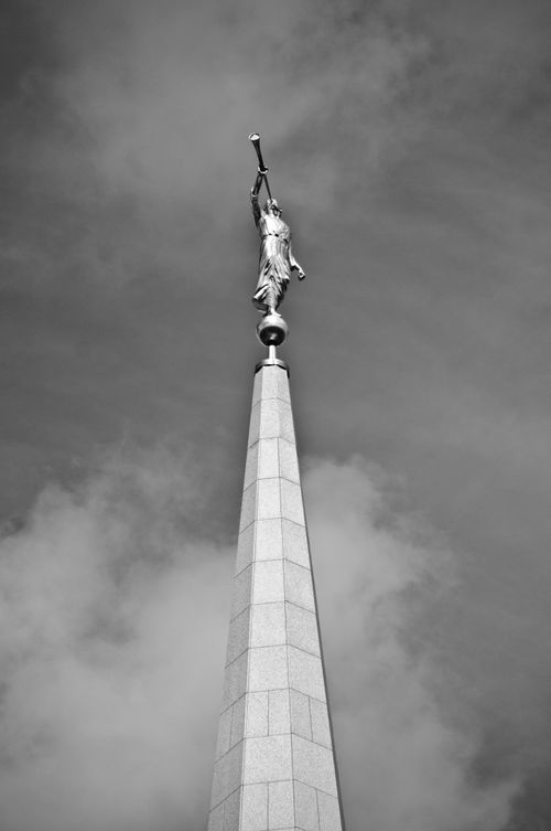 A black-and-white image showing the statue of the angel Moroni on top of the Preston England Temple with clouds in the background.