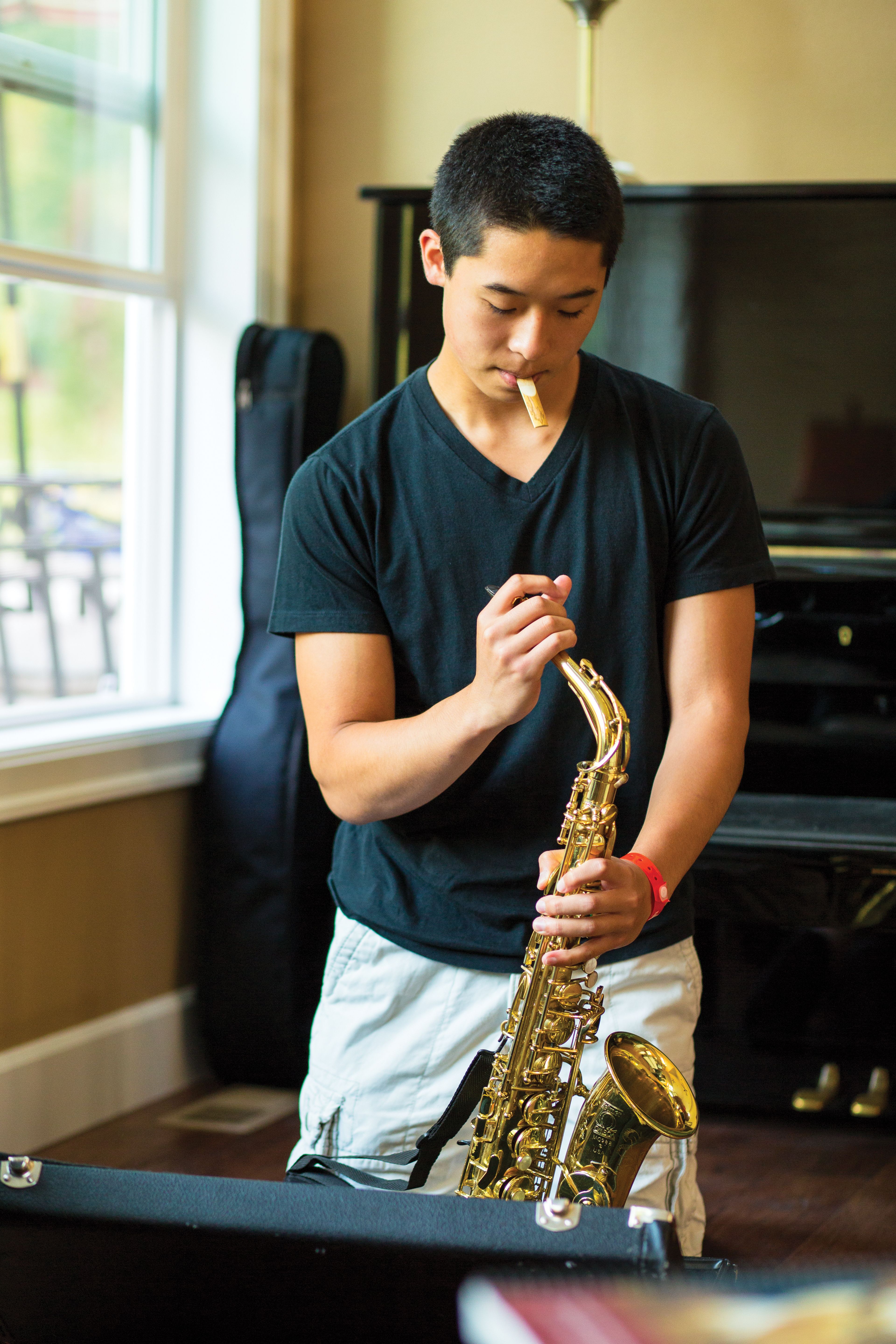 A young man prepares to put a reed on his saxophone.