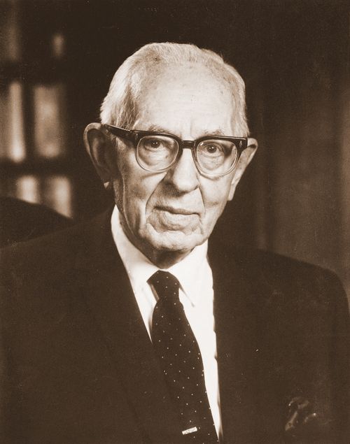 A formal portrait of the prophet Joseph Fielding Smith in a dark suit, a tie with white specks, and glasses.