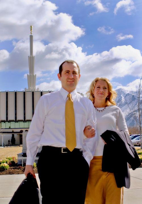 A couple walking with linked arms outside the Provo Utah Temple on a sunny day.