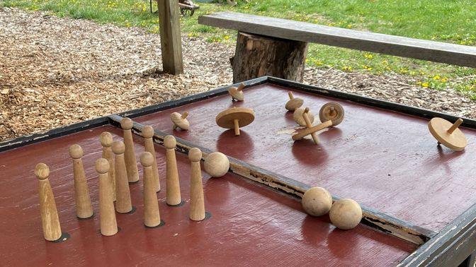 A dark red table with wooden bowling pins, balls, and spinning tops.