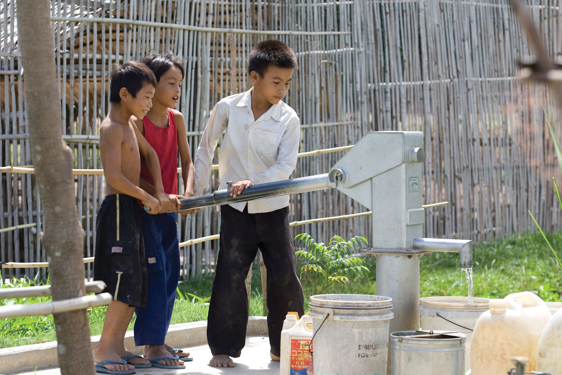 Three young boys pumping water from a hand-operated pump in Cambodia.