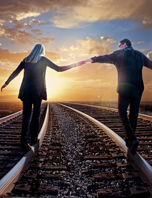 A couple holding hands and walking on railroad tracks.