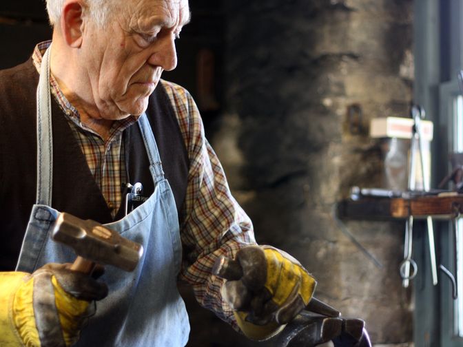 A man wearing an apron and gloves. He is holding a hammer and chisel in his hands.   