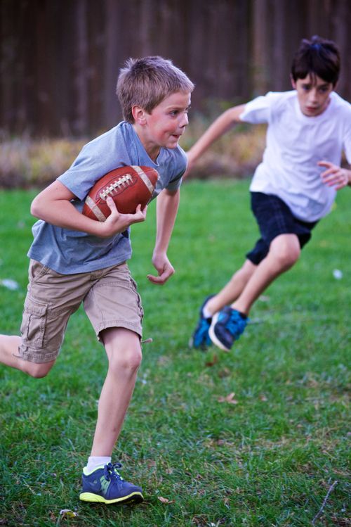 Two boys run through a field while playing football.