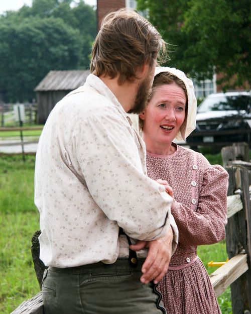 An actor from the Nauvoo Pageant leaning against a wooden fence and turning to look at an actress who is talking to him.