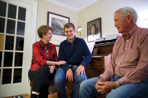 A couple sitting in a living room with their teenage grandson.