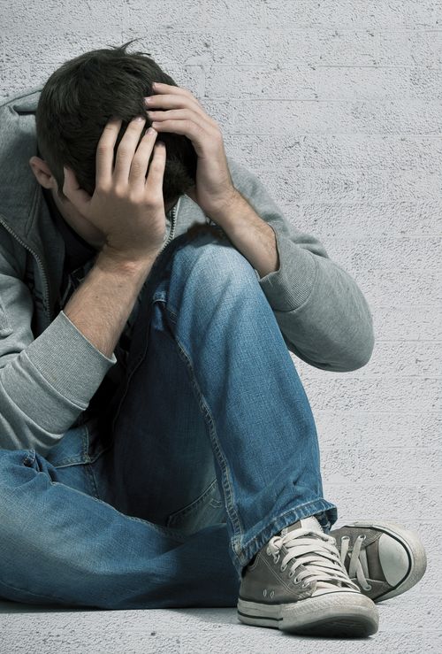 A young man sitting on the ground with his head in his hands. photo of young man covering head