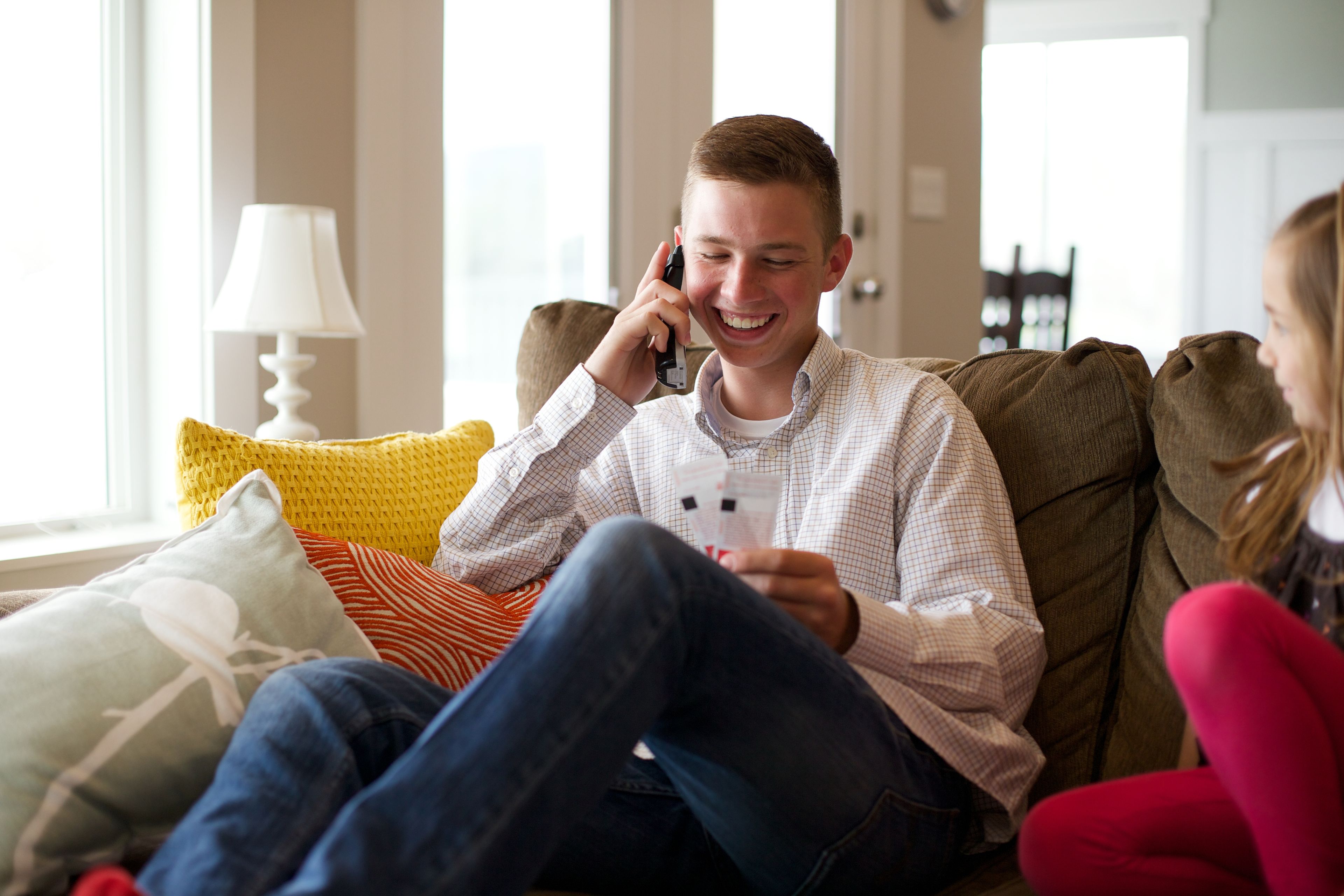 A young man sits on a couch and talks on a phone.