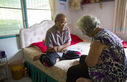 An older couple sitting on their bed in Thailand praying together.
