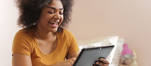 Young woman sits in her bedroom with an iPad or tablet in her hands