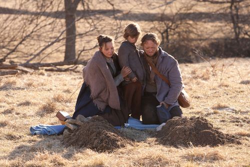 A pioneer couple and their young child at the new graves of their other children.