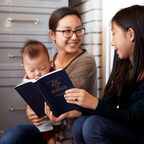 een glimlachende vrouw leest samen met haar kinderen in de Schriften