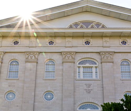 A detail of the Nauvoo Illinois Temple, with sunshine over the roof and the words “Holiness to the Lord: The House of the Lord” engraved on the building.