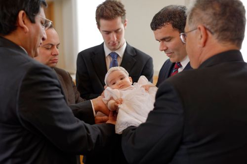 A group of men in suits holding and blessing an infant.