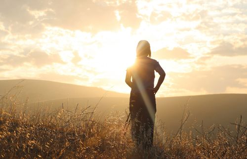 Een vrouw staat in een veld en kijkt naar de zon