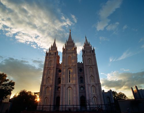 The front of the Salt Lake Temple in the evening, with the sun setting behind it and a view of the sky.
