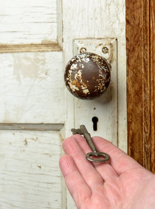 A hand holding a key in front of a keyhole.