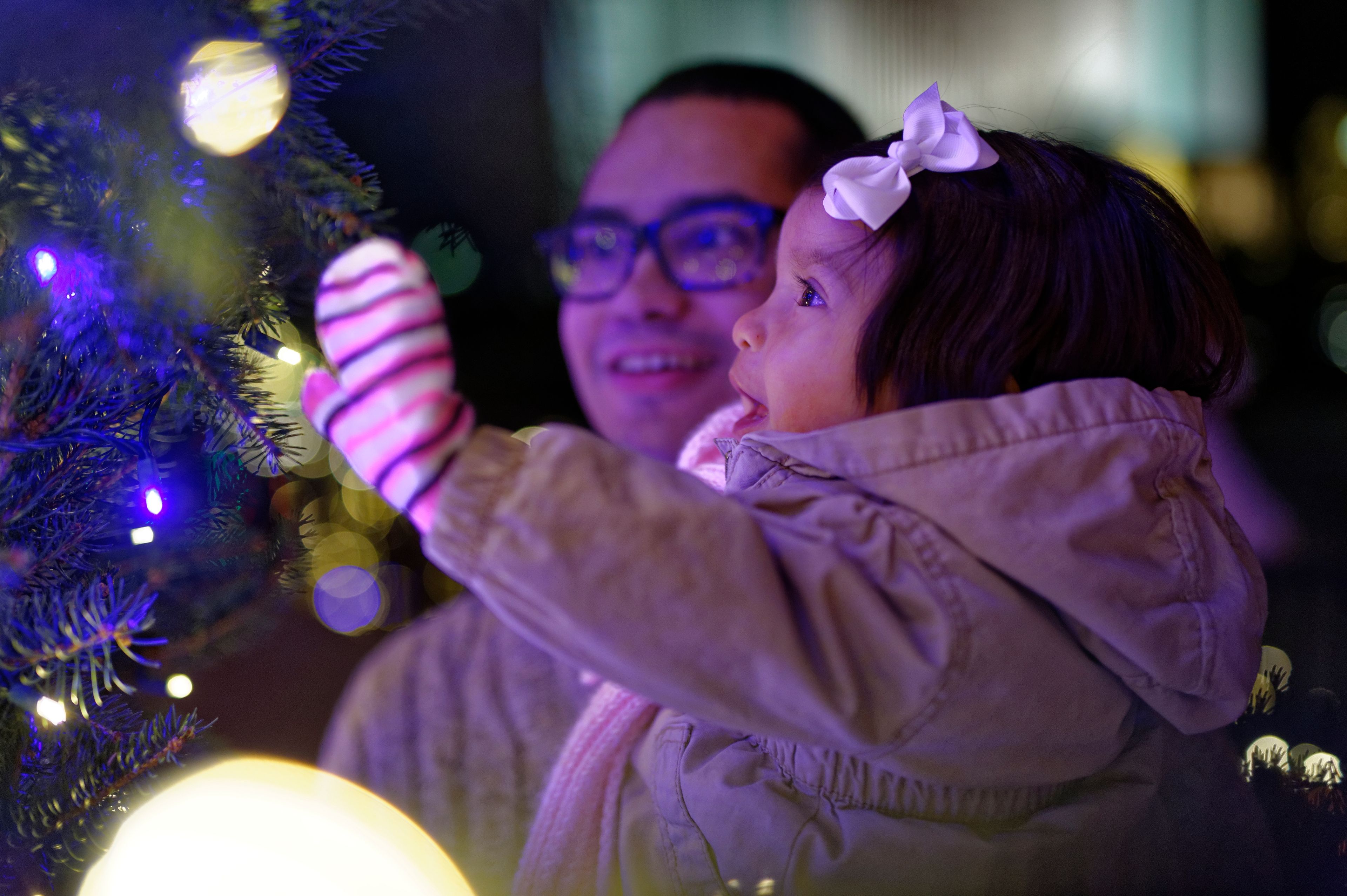 A father holding his young daughter while looking at the Christmas tree.