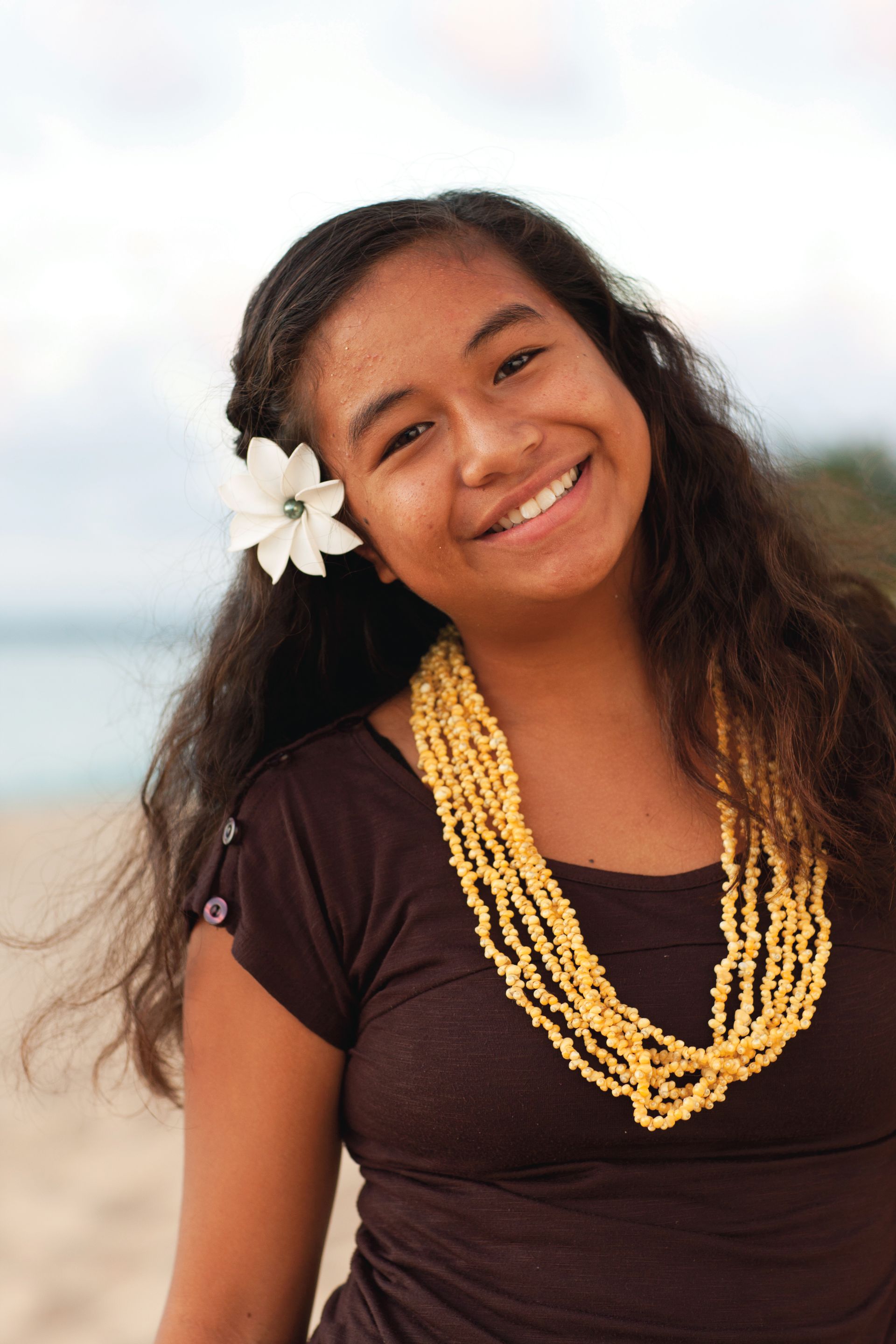 A young woman outdoors in Hawaii, with a flower in her hair, smiling.