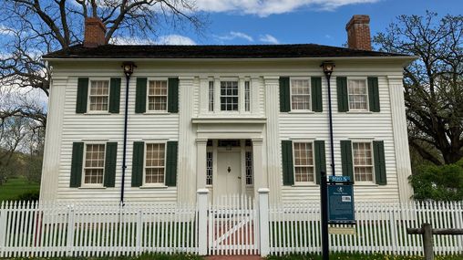 A large white clapboard home with a center entrance and chimneys on both ends.