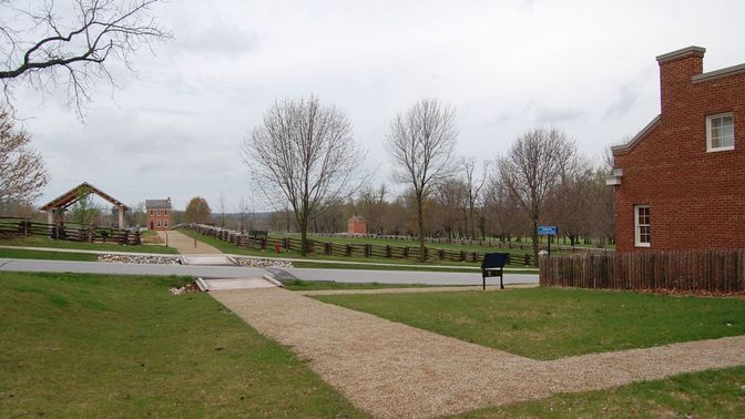 Grassy landscape with brick buildings, trees, and pathways.