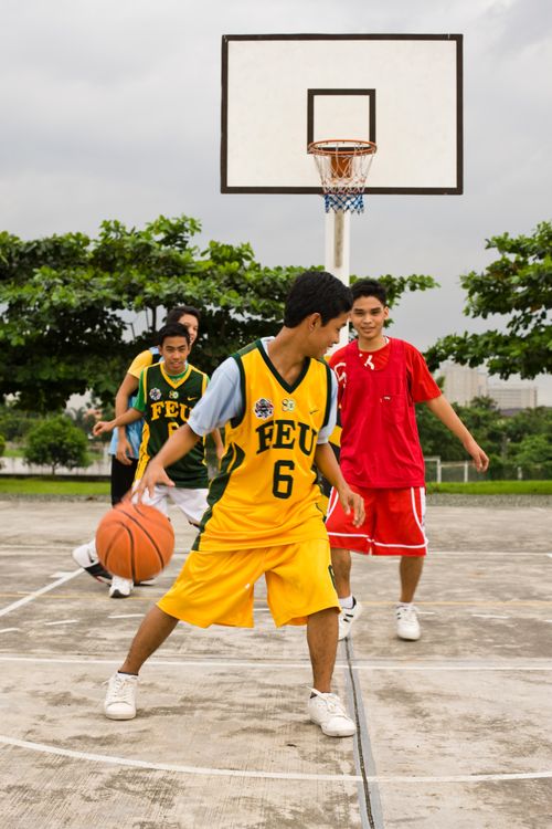 Four teenage boys in jerseys playing basketball on a court outside.