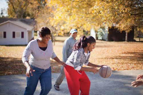 A mother and father play basketball with their teenage children in the driveway.