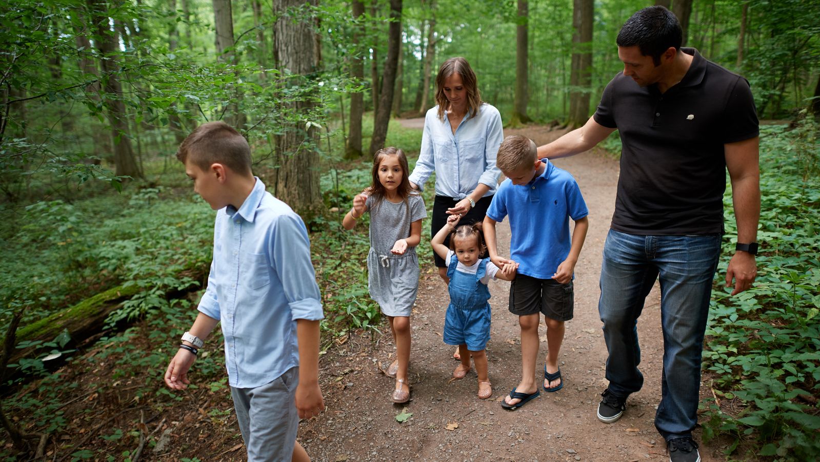 Various people walk the paths around the Sacred Grove. There are lots of trees around and everything is very green. The families are all walking on dirt pathways.