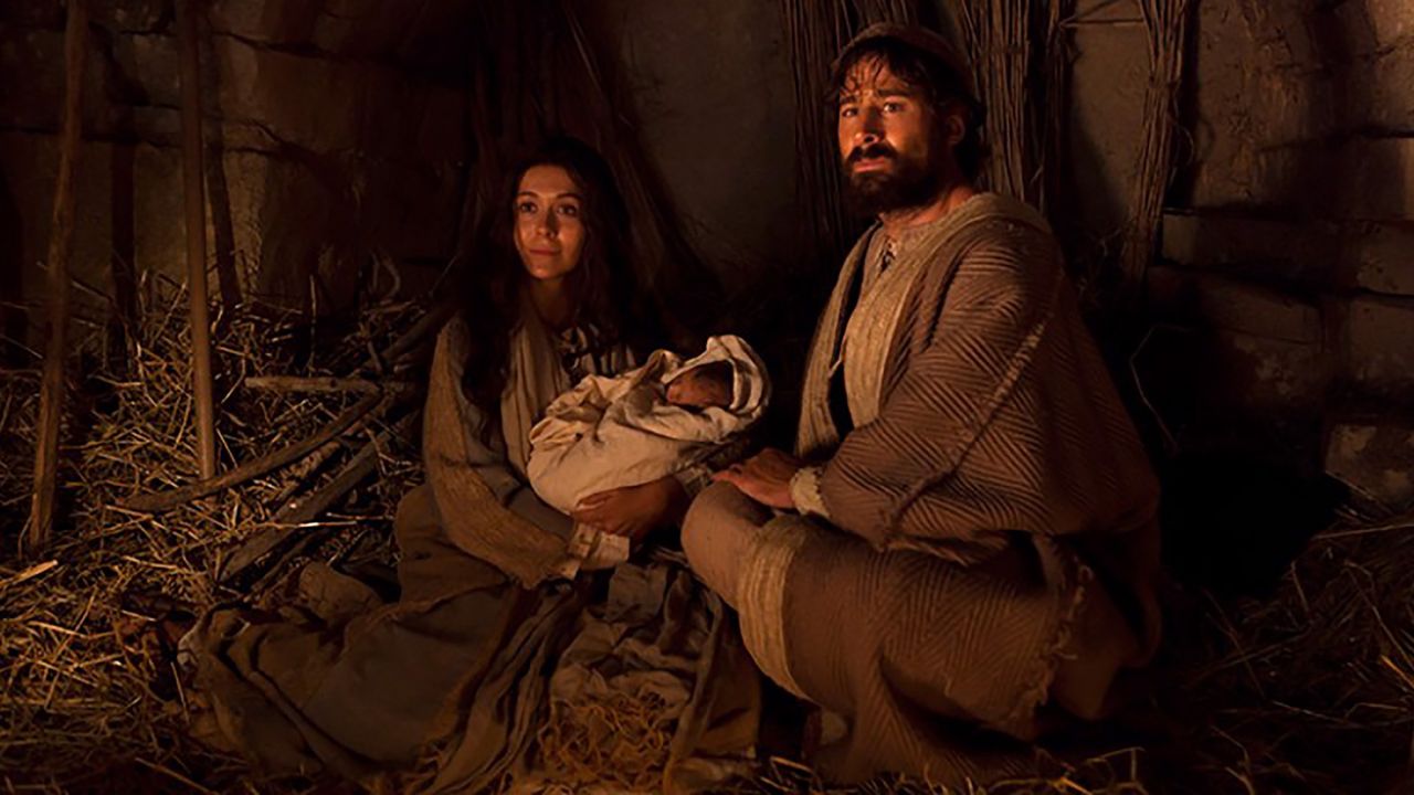 Mary and Joseph hold the newborn baby Jesus in a stable at Bethlehem while shepherds come to worship the Lord