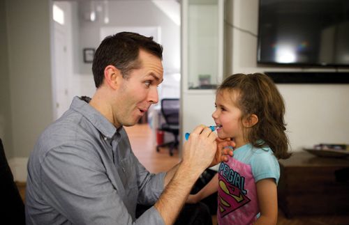 一位父親幫女兒刷牙。