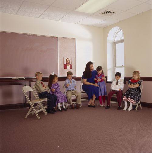 A girl praying in a Primary class, with five other classmates and one female teacher.