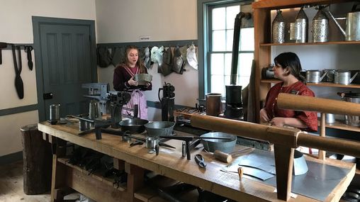 Two sister missionaries inside a historic home interacting with the artifacts.