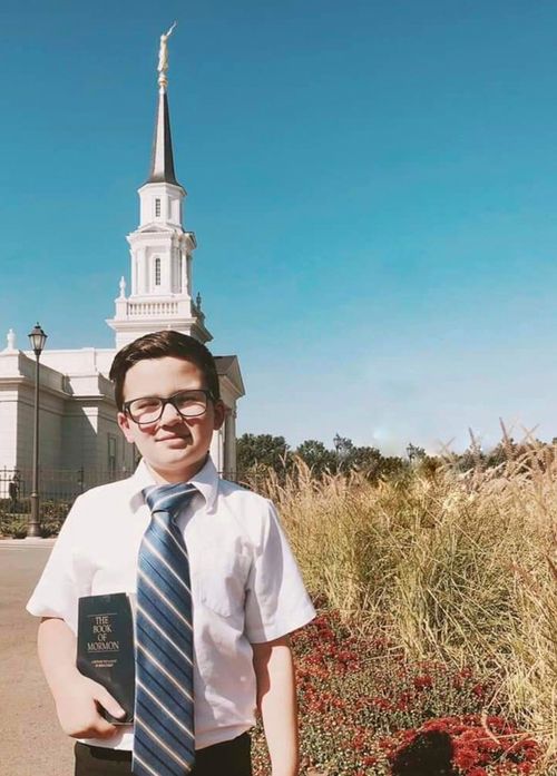 Henry Tillotson wearing a white shirt and tie is holding a Book of Mormon while standing in front of the Hartford Connecticut Temple.