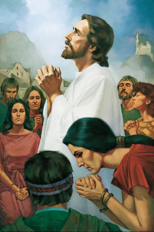 Jesus Christ in white robes, looking upward and standing amid a group of people in the Americas while they all pray together.