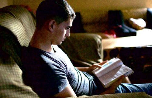 ung vuxen man sitter på en soffa och läser skrifterna