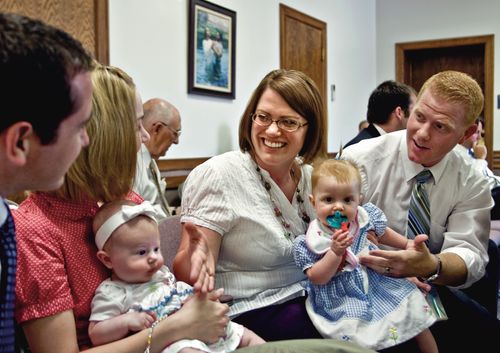 A young couple with a baby are talking to another young couple as they sit in a classroom.