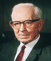 Portrait of President Joseph Fielding Smith sitting in a black leather chair in front of a book shelf. He is holding a copy of the scriptures in his hands.